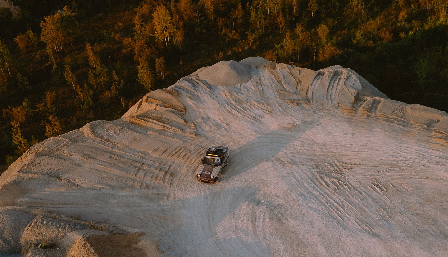 Porsche 944 Dakarista w terenie – widok z góry Klasyczne Porsche 944 Dakarista podczas jazdy po szutrowym terenie o zachodzie słońca