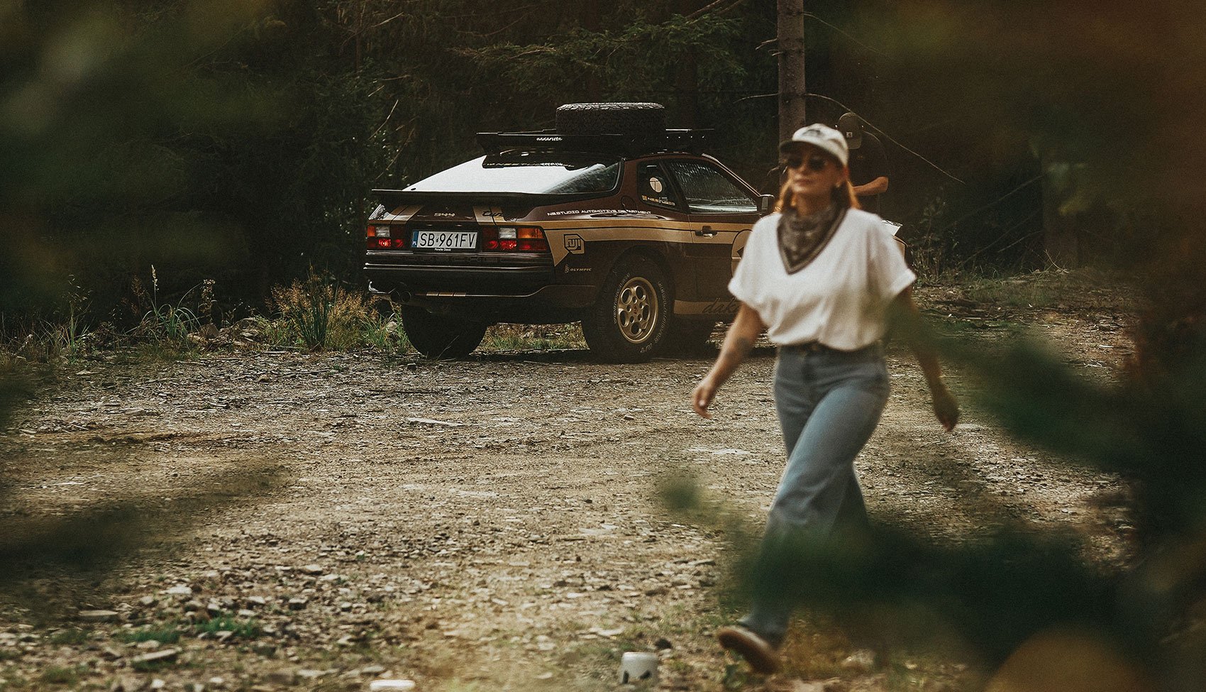 Porsche 944 Dakarista w lesie Porsche 944 Dakarista zaparkowane w lesie, kobieta w kapeluszu odchodzi w kadrze