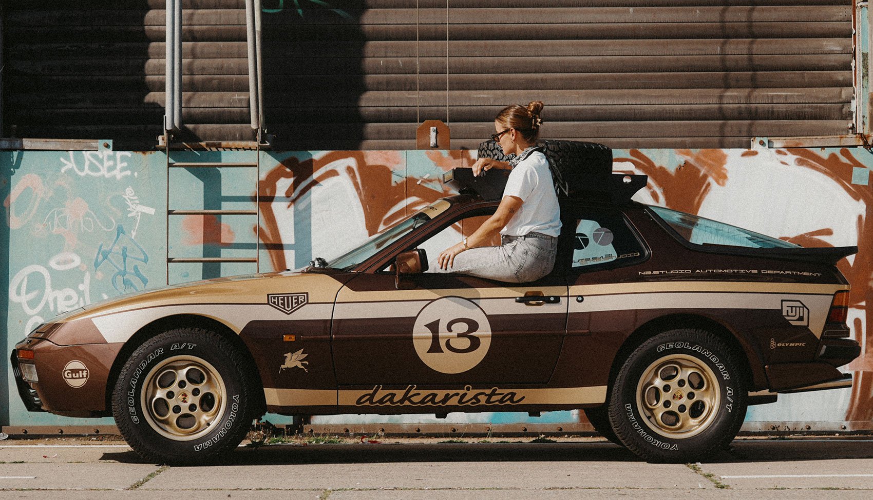 Porsche 944 Dakarista i właścicielka na tle graffiti Kobieta siedząca na dachu Porsche 944 Dakarista w miejskim otoczeniu z kolorowym graffiti