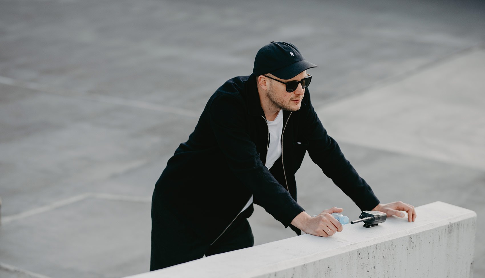 Tomek Mąkolski w pracy Fotograf podczas pracy w miejskiej przestrzeni – skupiony nad aparatem, uchwycony w minimalistycznym, industrialnym otoczeniu.