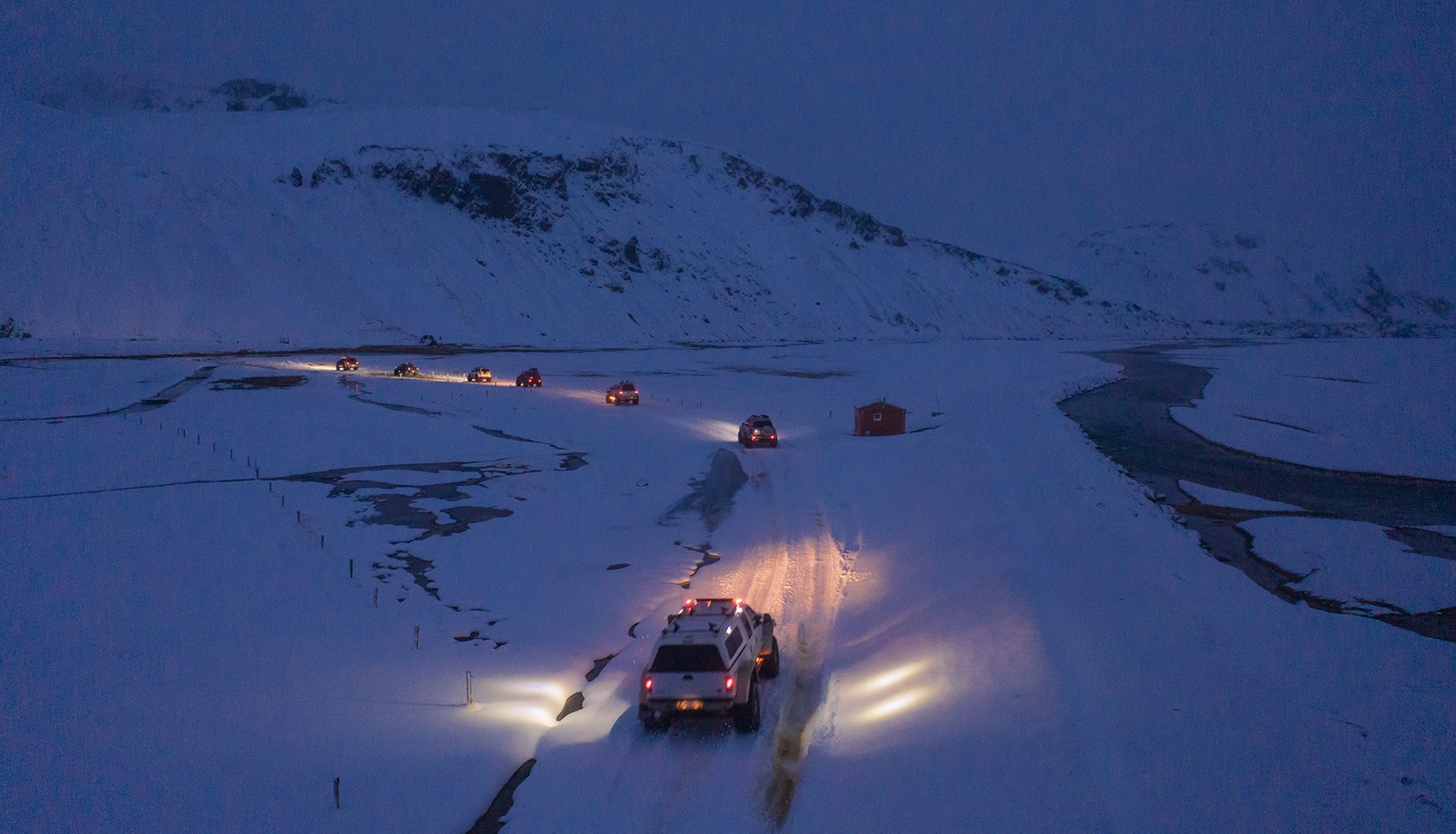 Nocna przeprawa przez śnieżne góry Samochody terenowe jadące wąskim, ośnieżonym szlakiem po zmroku, oświetlone reflektorami