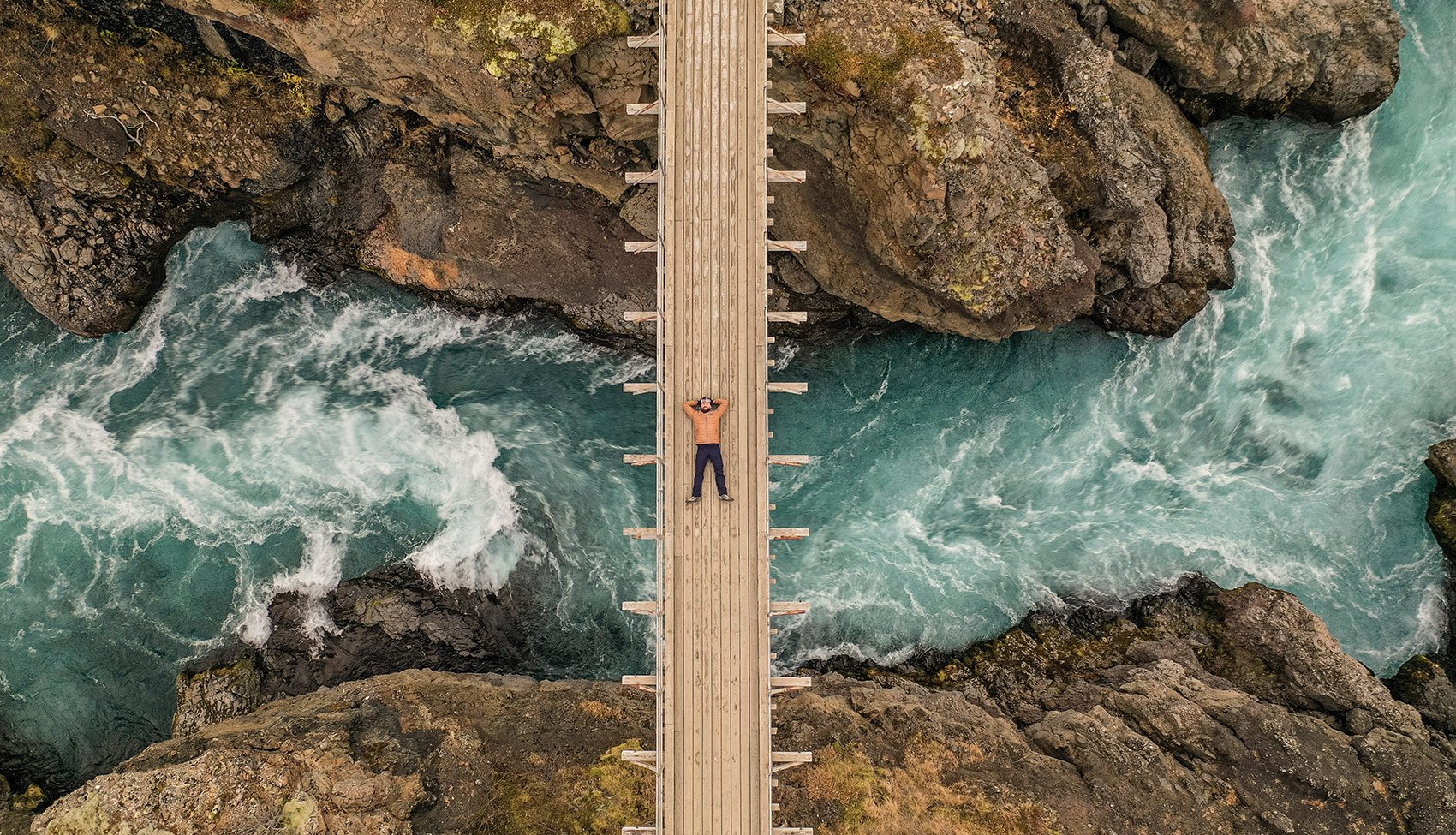 Ujecia z lotu ptaka to domena Pawła Mężczyzna leżący na drewnianym moście nad rwącą, błękitną rzeką – zdjęcie z drona