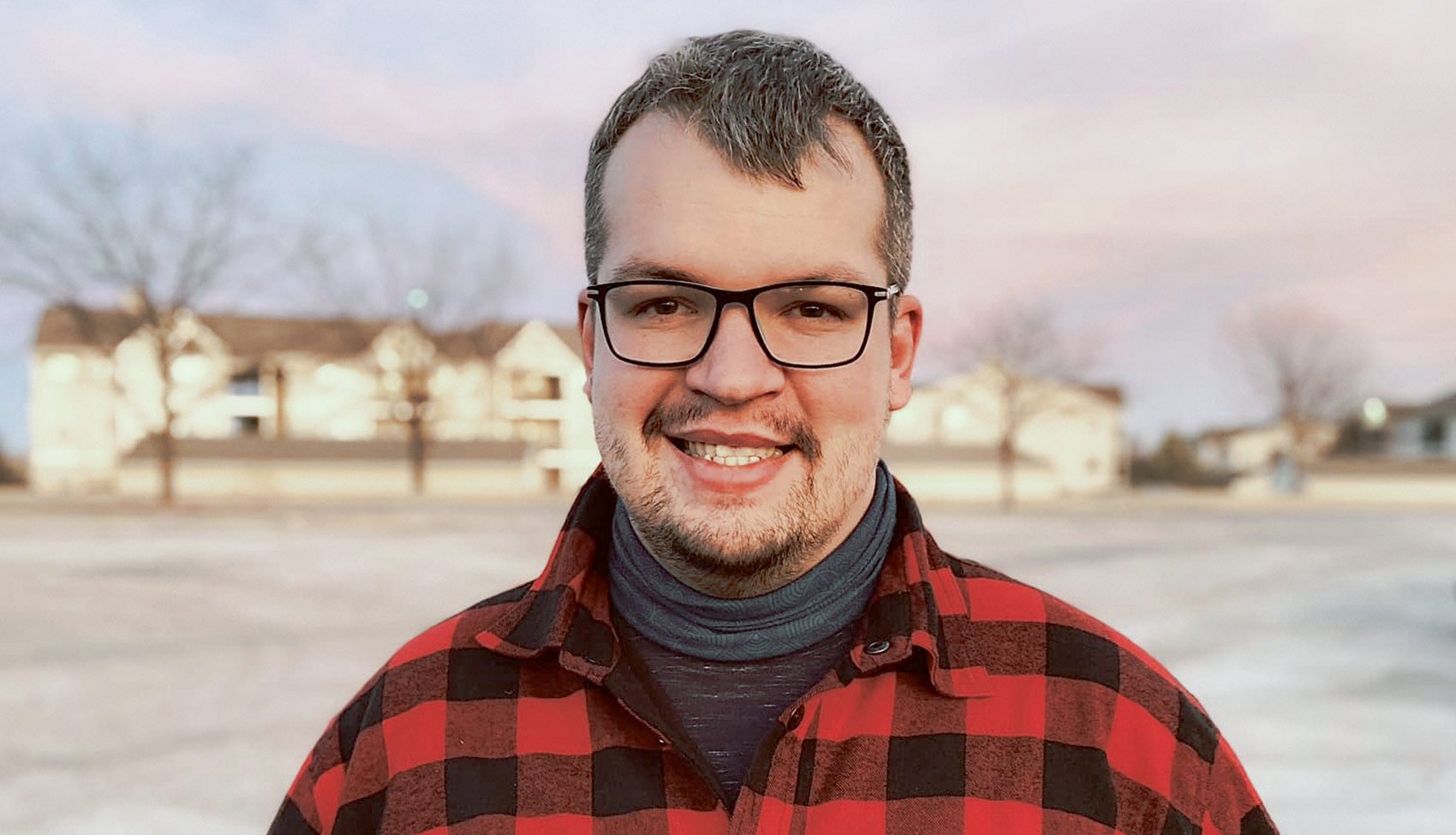 Portret Pawła Sudoła Paweł Sudoł – fotograf i operator drona w czerwonej koszuli, uśmiechnięty, w plenerze