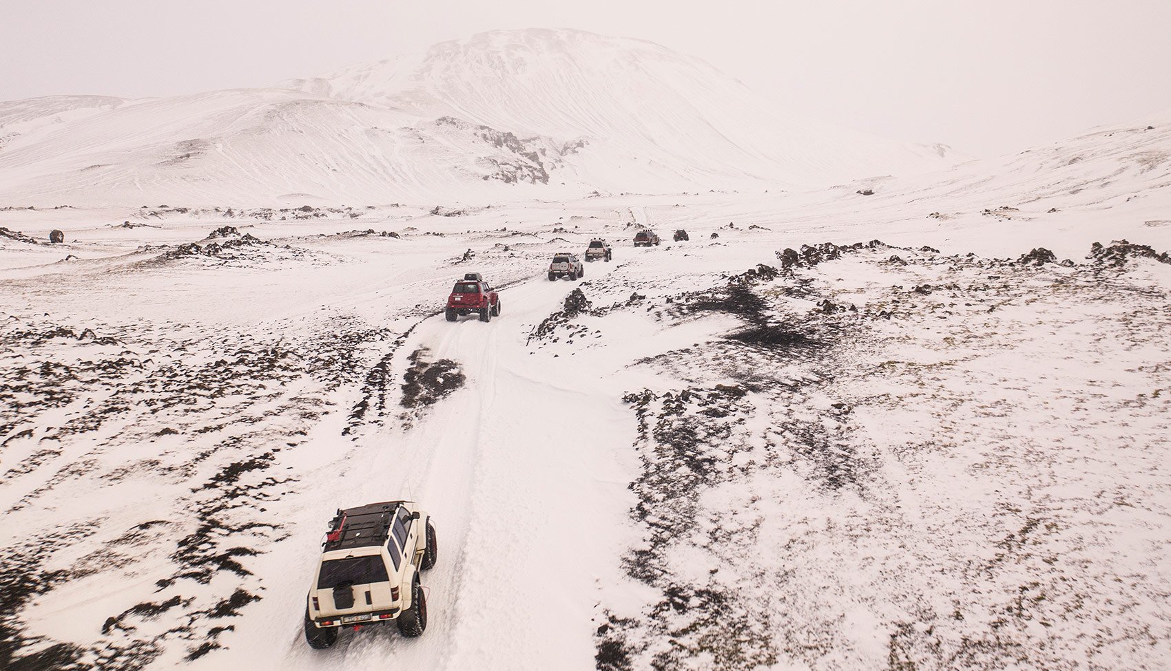 Konwój terenowych aut w zimowej scenerii Kolumna samochodów terenowych pokonująca ośnieżoną drogę nocą, ujęcie z drona