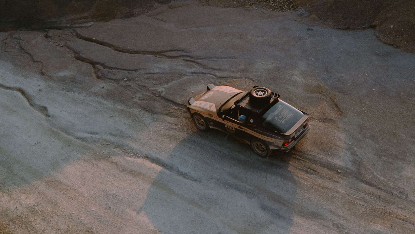 Klasyczne Porsche 944 Dakarista podczas jazdy po szutrowym terenie o zachodzie słońca