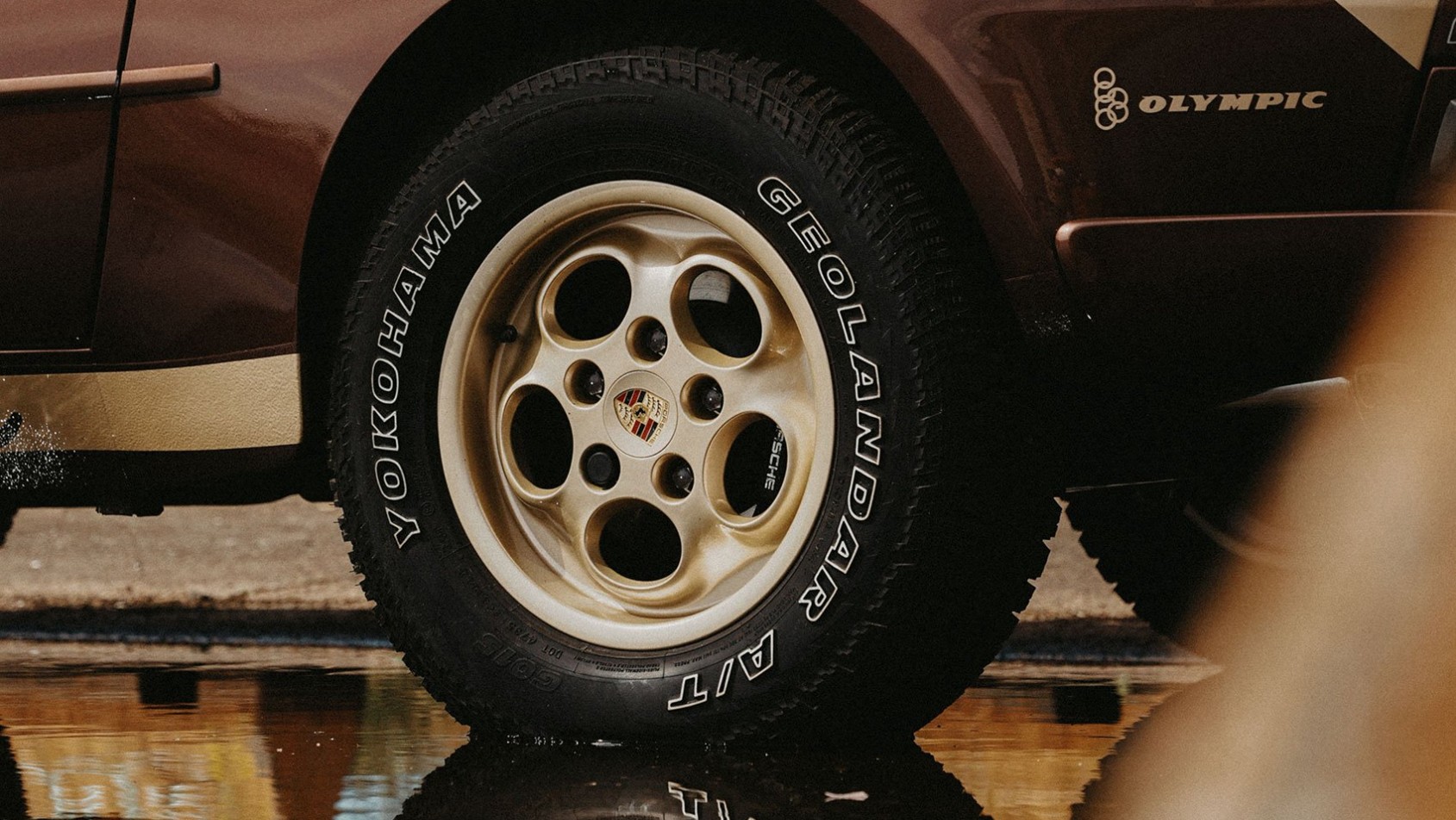 Zbliżenie na felgę Porsche 944 z oponą Yokohama Geolandar A/T – odbicie w kałuży