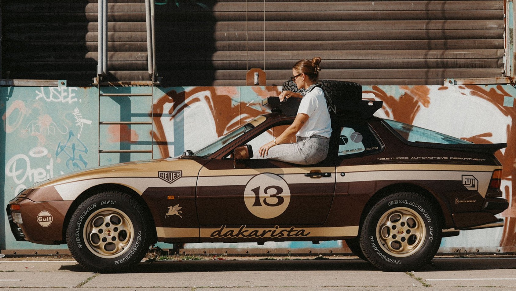 Kobieta siedząca na dachu Porsche 944 Dakarista w miejskim otoczeniu z kolorowym graffiti