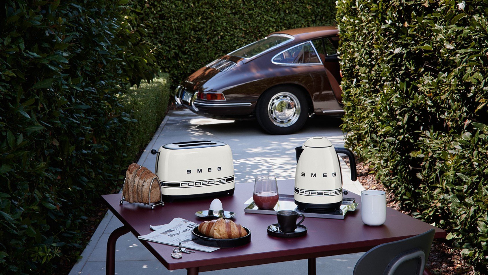 Toster i czajnik Porsche x SMEG Carrara White na stole obok klasycznego Porsche 911