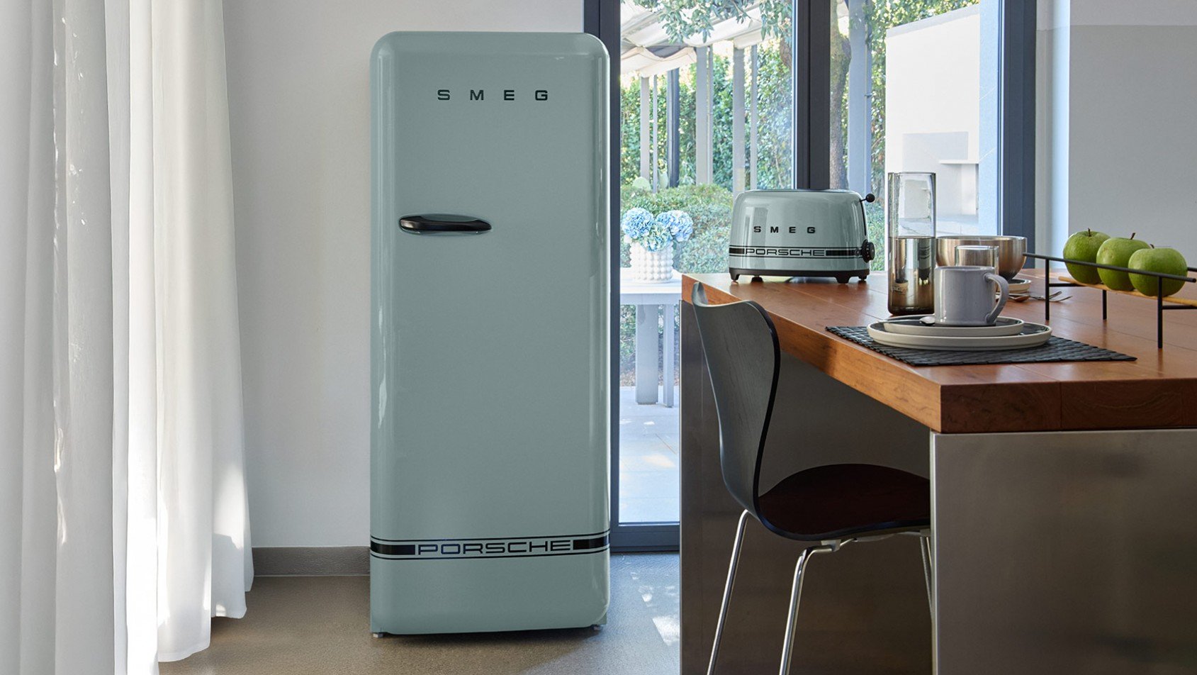 Lodówka i toster Porsche x SMEG Shade Green w minimalistycznym wnętrzu kuchni z drewnianym stołem