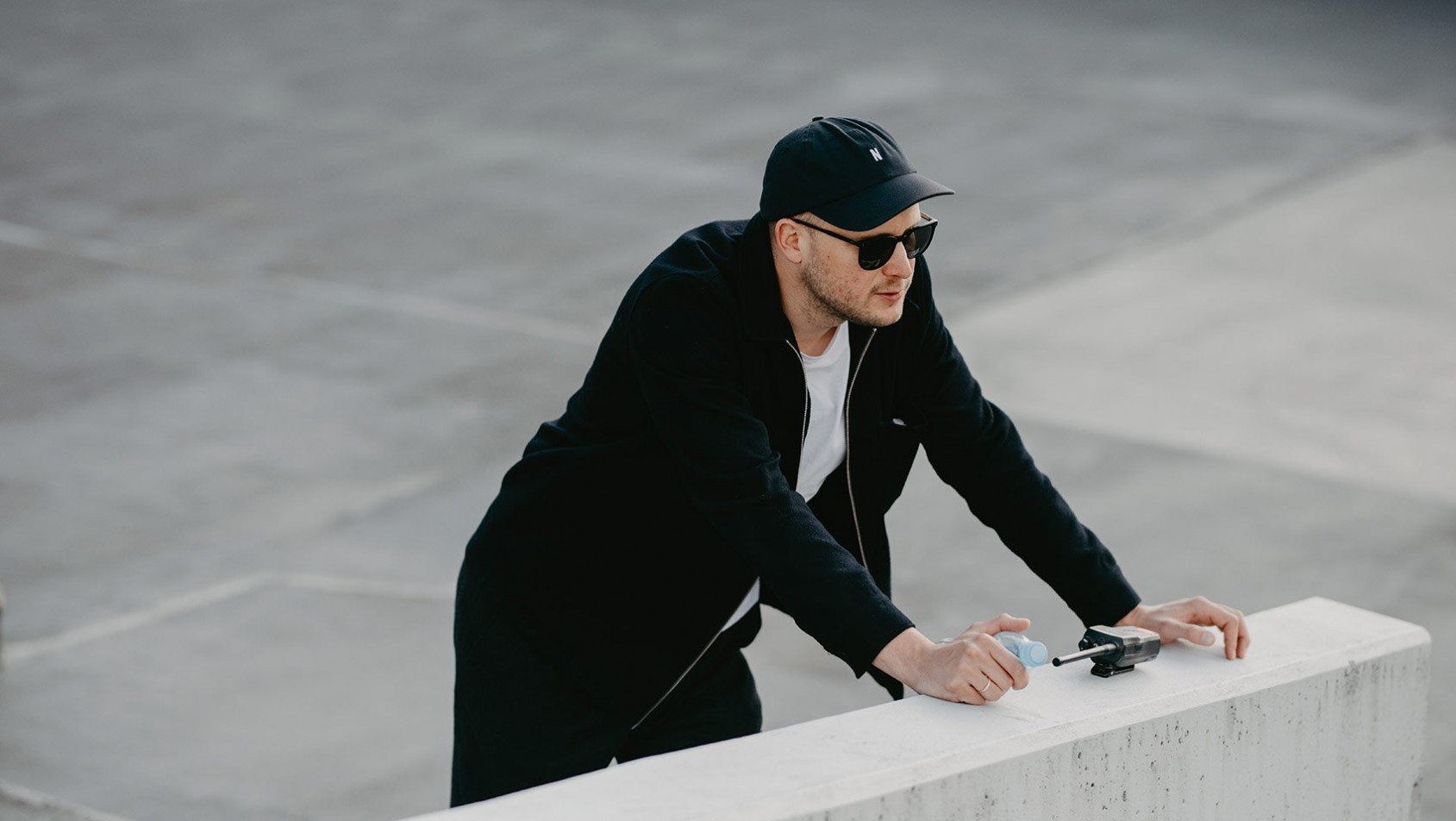 Fotograf podczas pracy w miejskiej przestrzeni – skupiony nad aparatem, uchwycony w minimalistycznym, industrialnym otoczeniu.