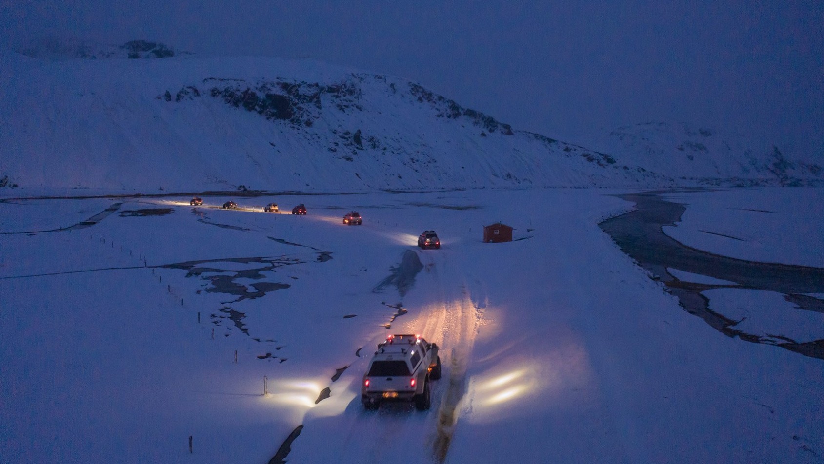Samochody terenowe jadące wąskim, ośnieżonym szlakiem po zmroku, oświetlone reflektorami