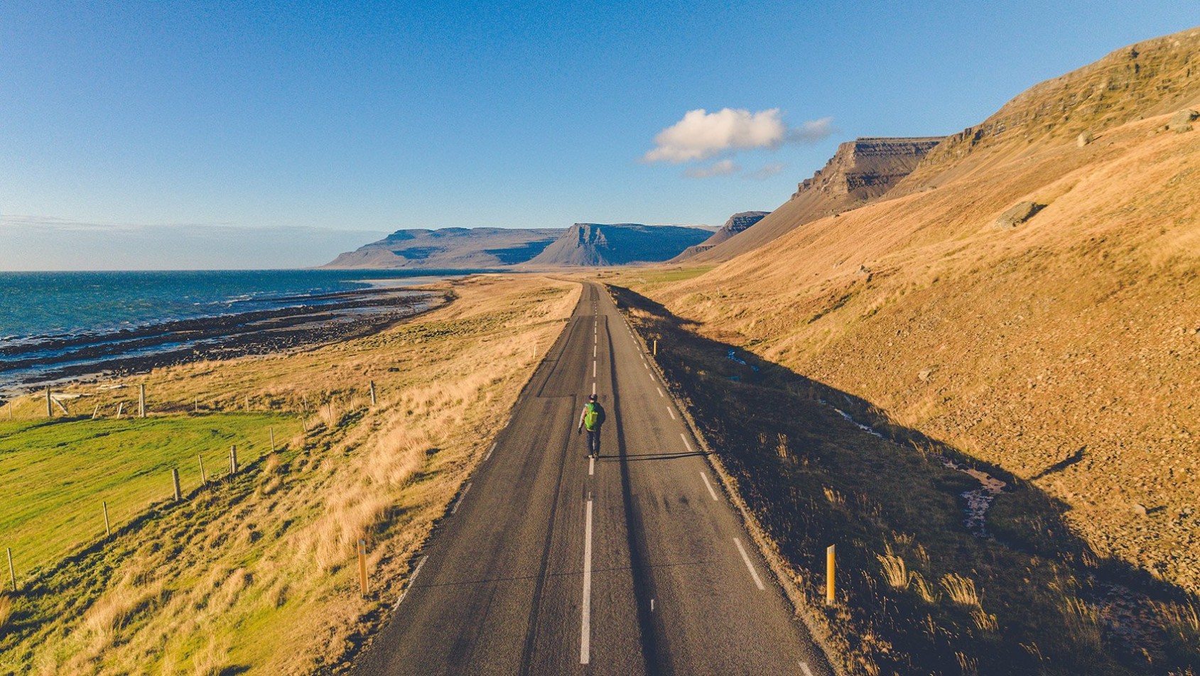 Osoba idąca samotnie pustą drogą wśród gór i oceanu na Islandii, widok z góry