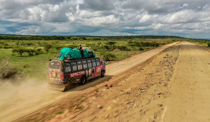 Ujęcie z drona przedstawiające barwny autobus jadący po pustynnej drodze w Afryce