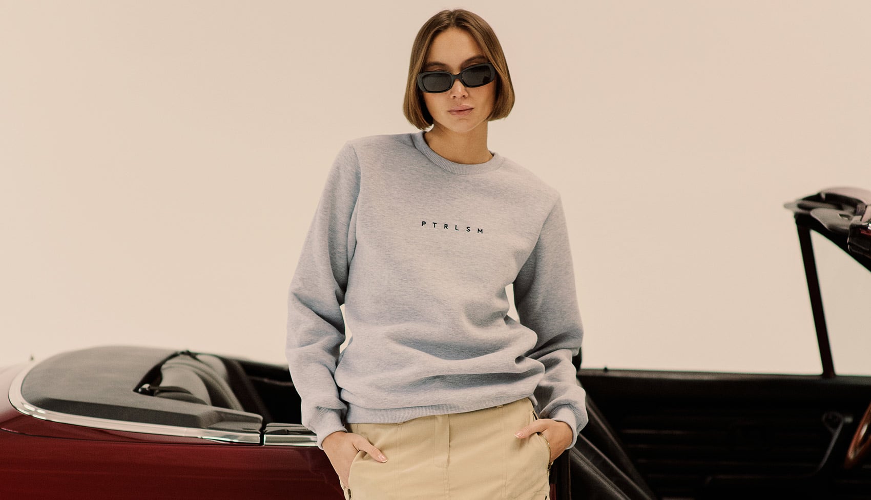 Sylwetka w szarej bluzie PTRLSM na tle klasycznego kabrioletu, minimalistyczna estetyka i motoryzacyjny kontekst