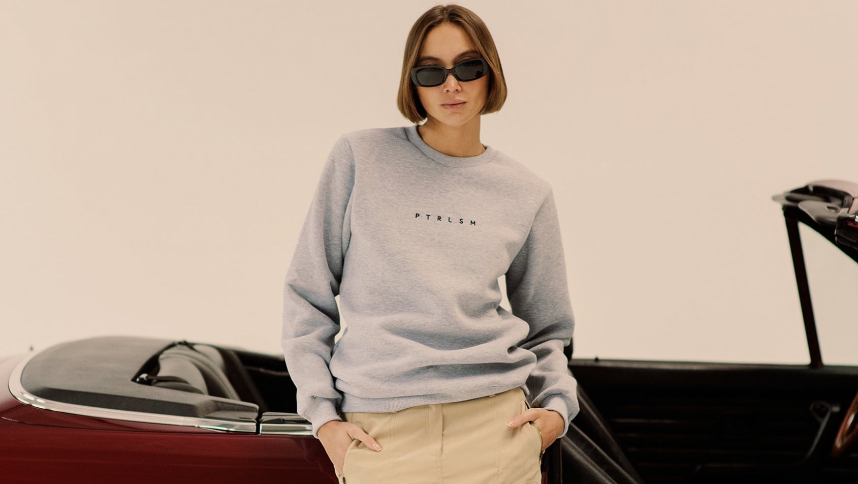 Sylwetka w szarej bluzie PTRLSM na tle klasycznego kabrioletu, minimalistyczna estetyka i motoryzacyjny kontekst