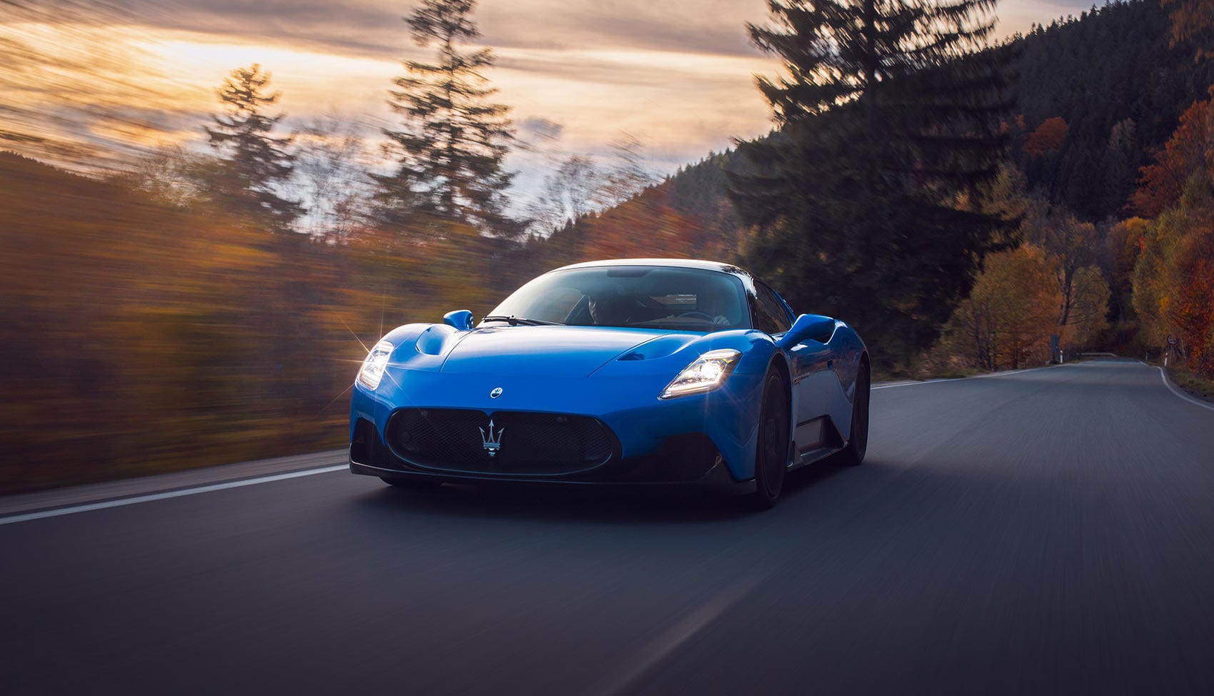 Sportowe Maserati jadące krętą drogą w&nbsp;jesiennym lesie