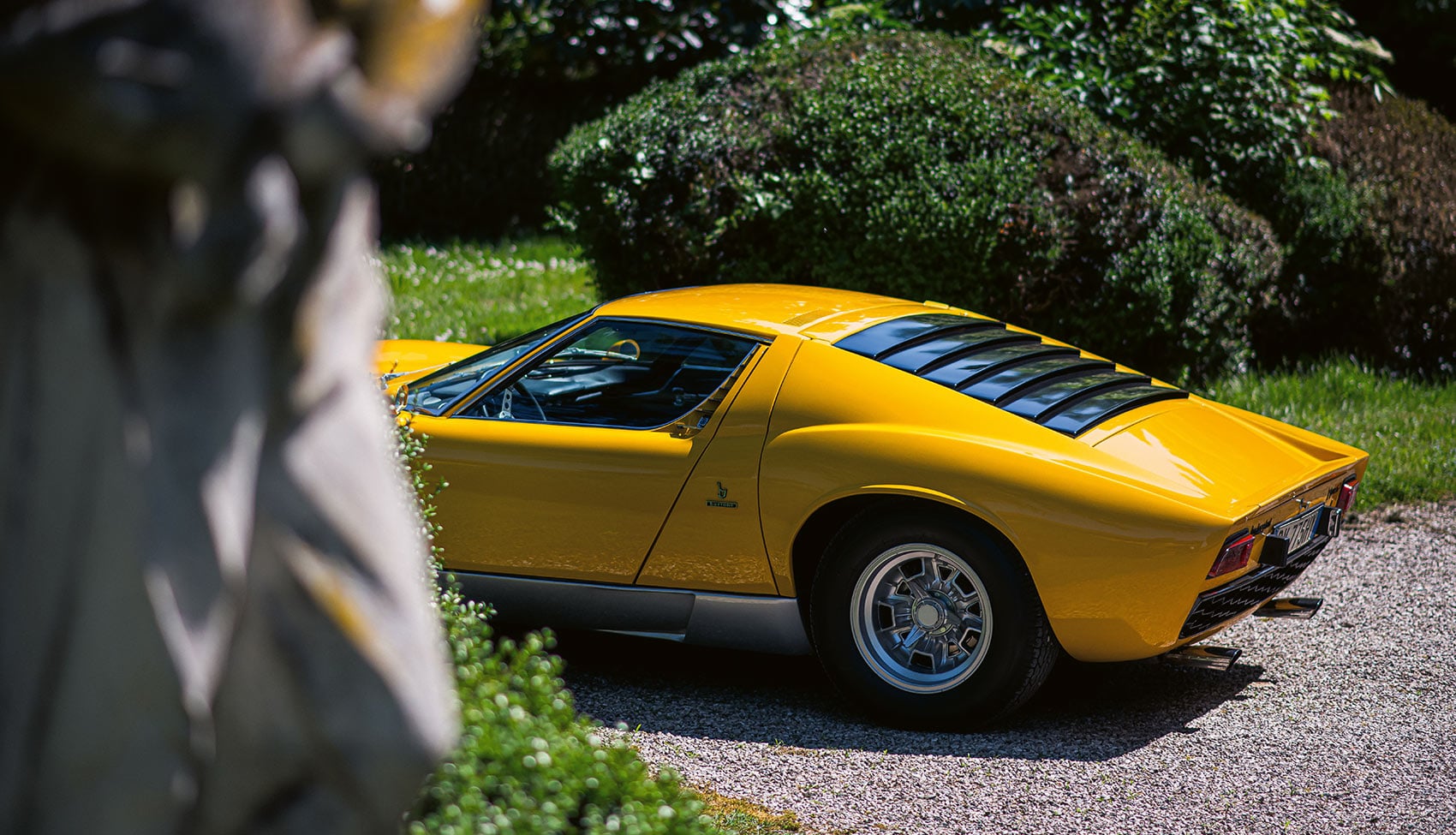 Żółte Lamborghini Miura P400 S widziane z&nbsp;tyłu w&nbsp;ogrodzie