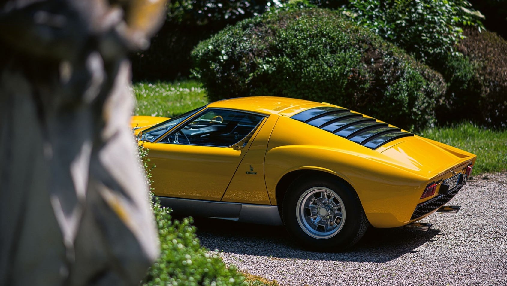 Żółte Lamborghini Miura P400 S widziane z tyłu w ogrodzie