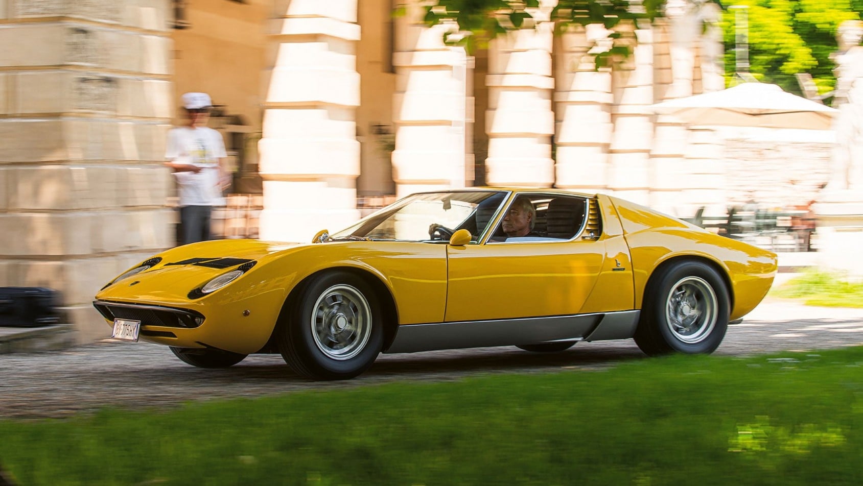Żółte Lamborghini Miura P400 S jadące obok zabytkowego pałacu